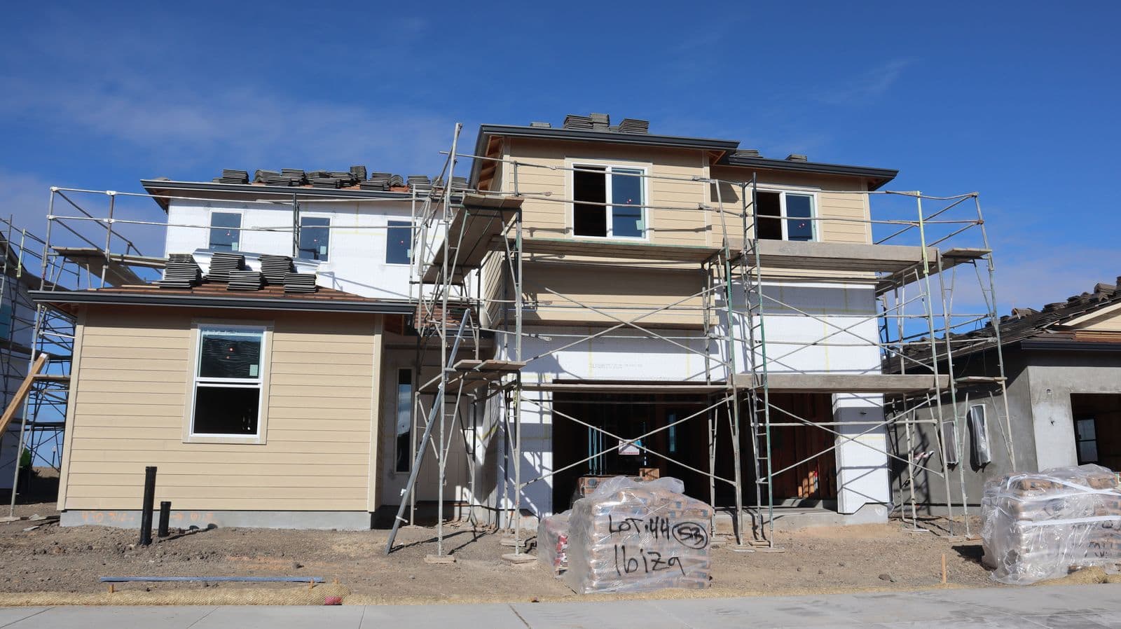 Two-story house under construction with scaffolding and part of its siding on